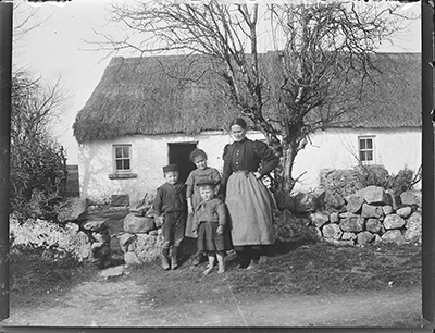 Woman and 3 children outside thatched cottage, probably Ahascragh, Co. Galway