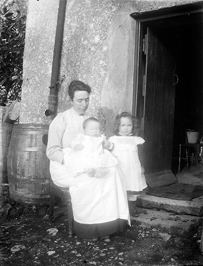 Woman seated at doorway with 2 children, 1912