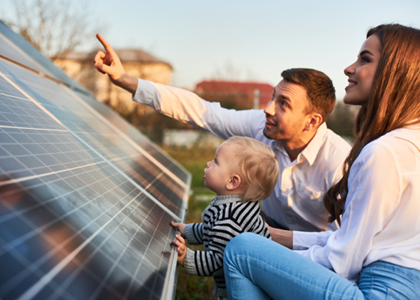 Kneeling man and woman showing a toddler a solar panel in autumn evening sunlight